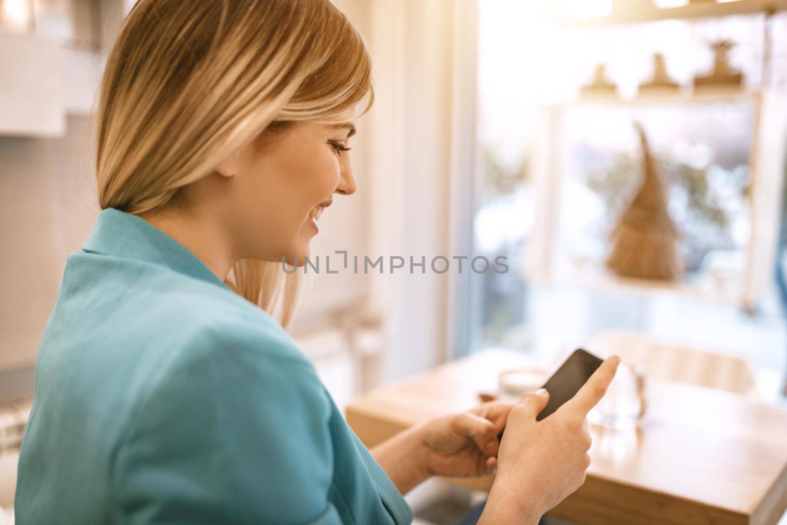 Young smiling businesswoman on a break in a cafe. He is drinking coffee and using smartphone. 