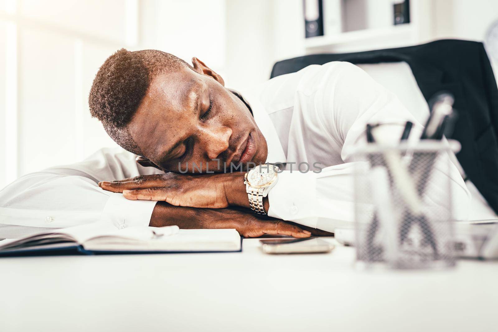 Tired African businessman is napping on desk next to documents late in the office.