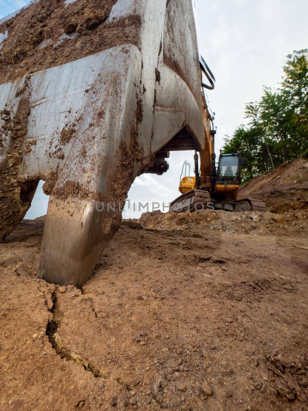 Industrial toothed digger bucket bite the ground, low angle view. Loader constraction excavator bucket close up.