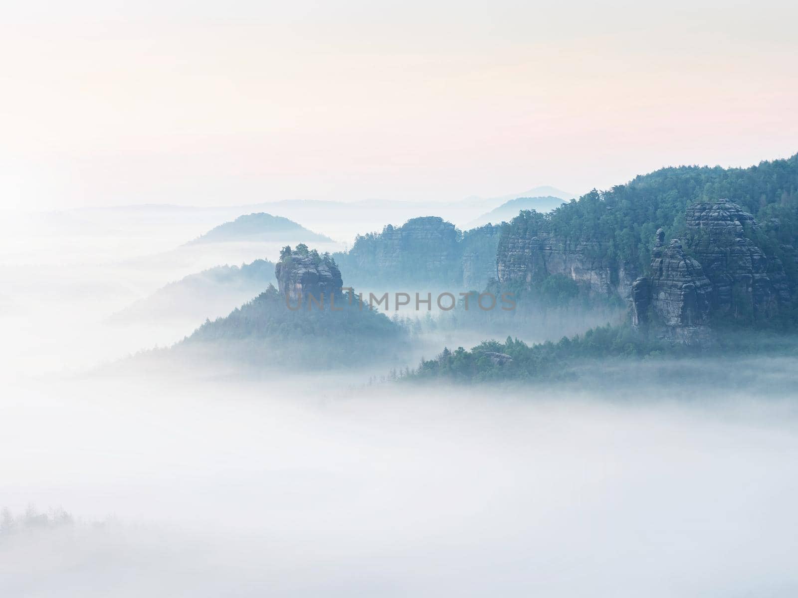 Panoramic misty view of forested Winterstein hinteres Raubschloss in Saxon Switzerland. Few minutes before sunrise
