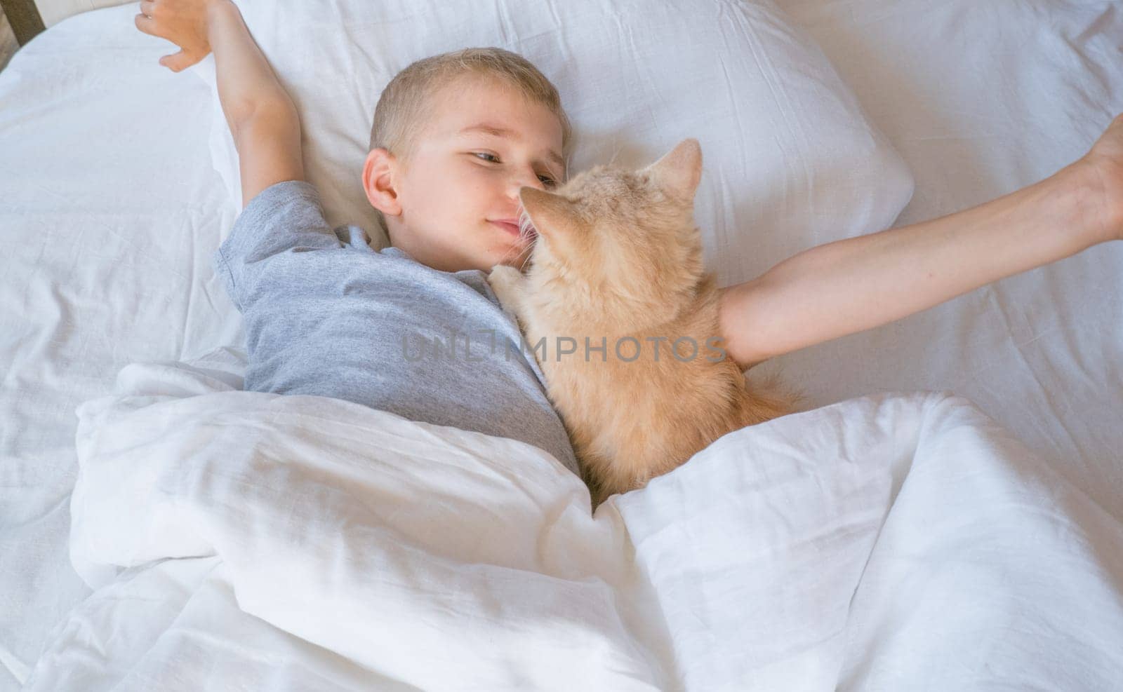 A child in bed cannot fall asleep, yawns, grimaces and plays with a ginger cat