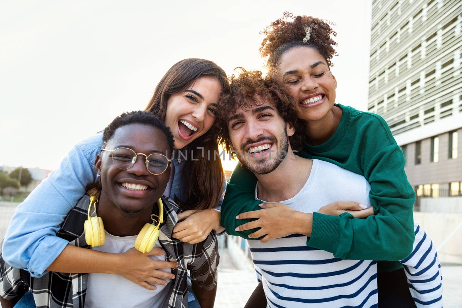 Multiracial happy friends having fun looking at camera. Young men piggy back ride female friends. Youth lifestyle concept.