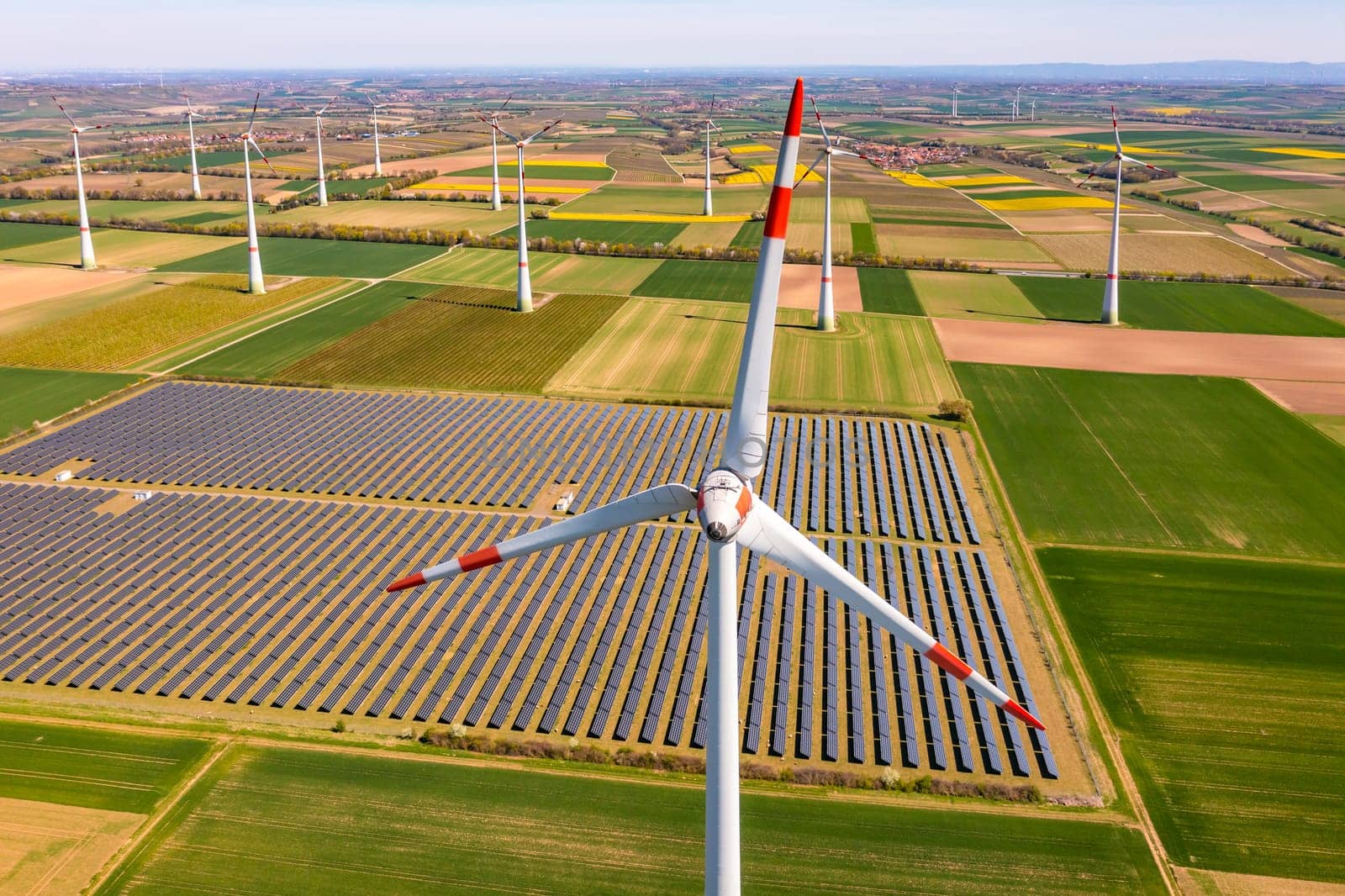 Aerial close-up view of a wind turbine in front of agricultural fields and photovoltaic panels of a solar park in energy crisis