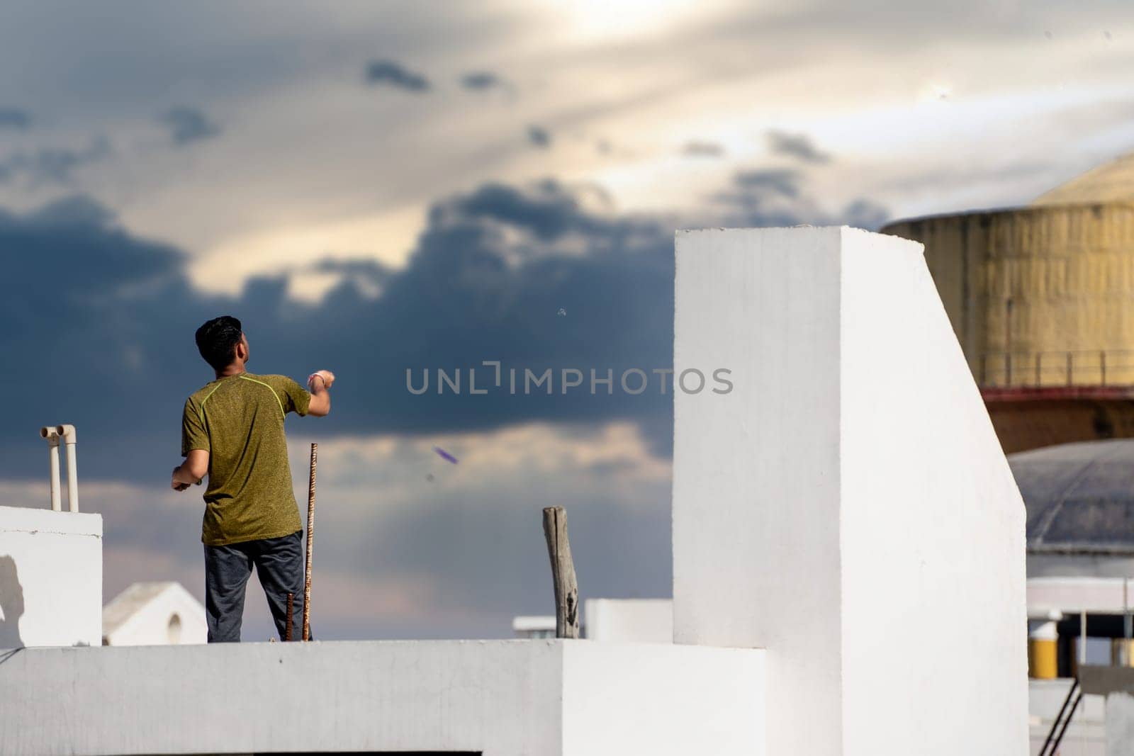 Jaipur, Rajasthan - 14th Jan 2023: Slow motion shot of man on roof of white building flying kite with multiple kites visible in background during the festival of sankranti, uttarayan and independence day