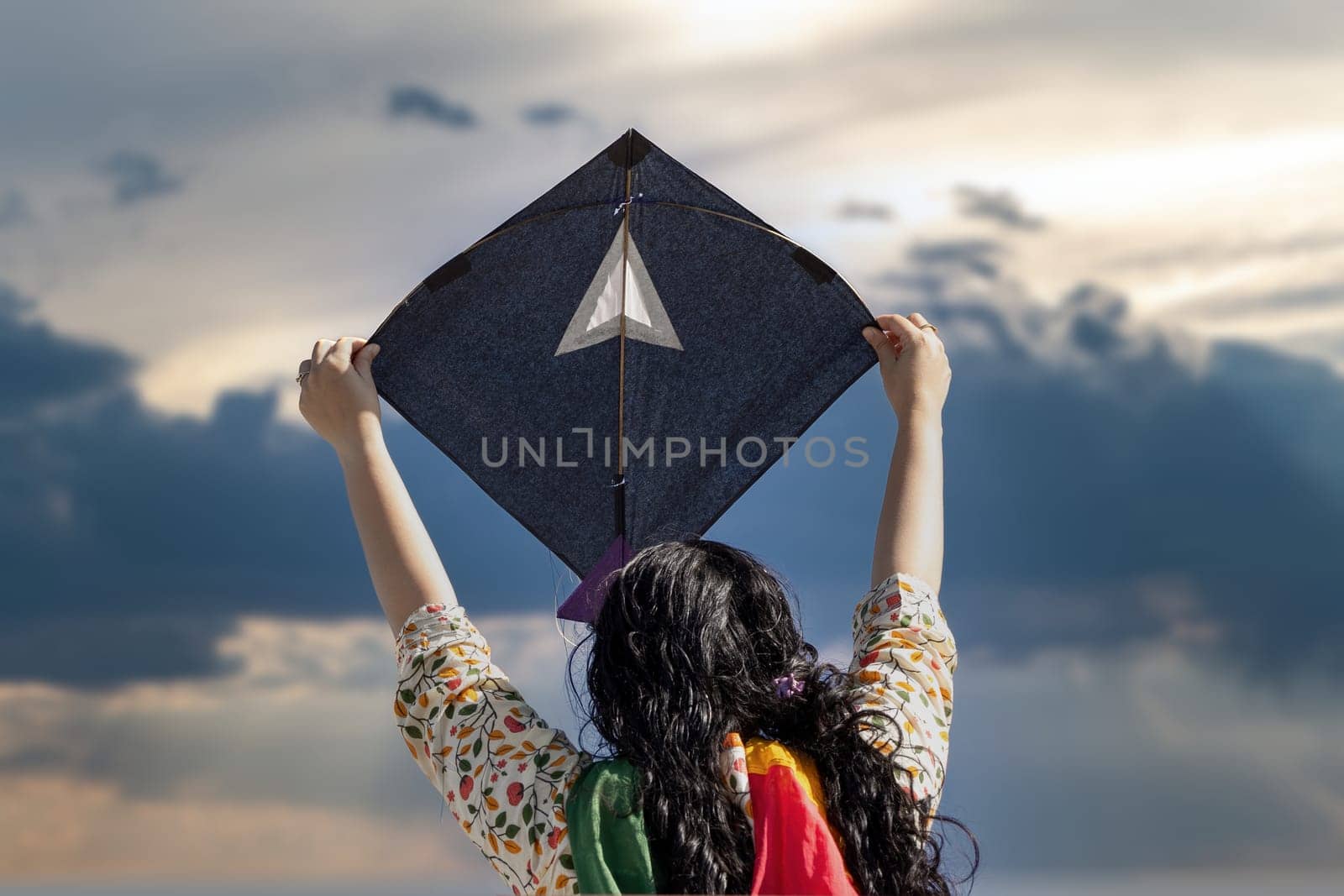 Young girl in traditional indian clothing holding black kite high above head launching it on sankranti republic independence day celebrations