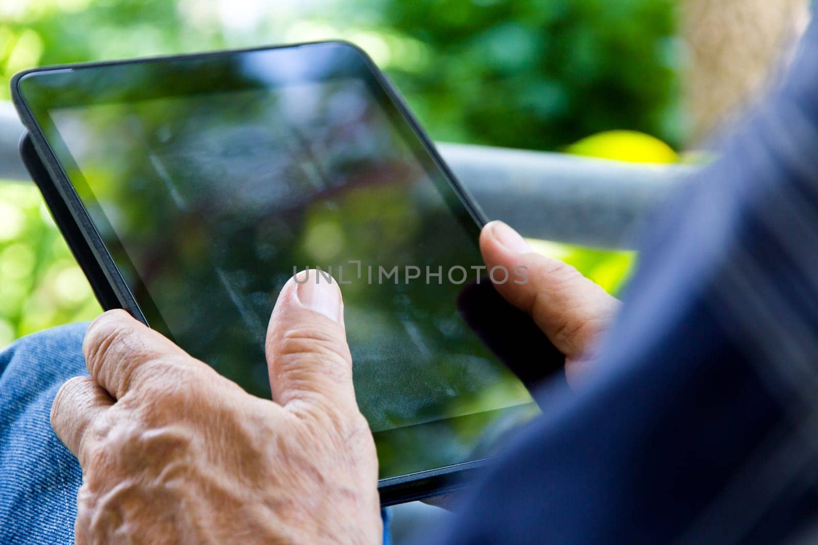 Senior man sitting outside reading E-book on his tablet.