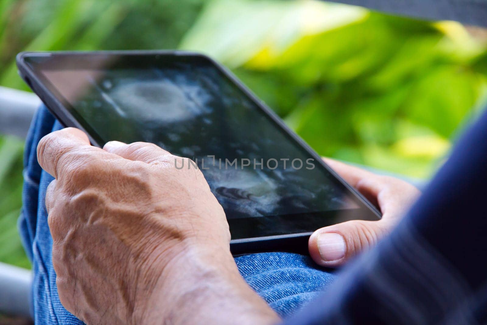 Senior man sitting outside reading E-book on his tablet.