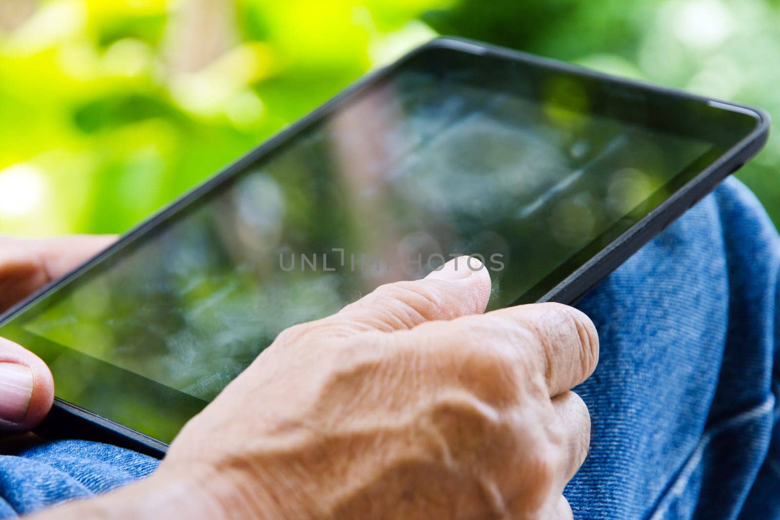 Senior man sitting outside reading E-book on his tablet. by ponsulak