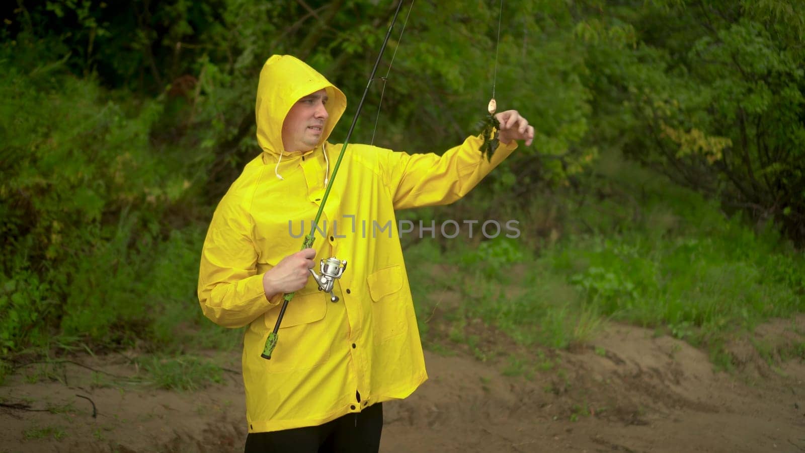 A young man in a yellow cloak with a hood is fishing on the shore. A joyful man caught seaweed on a hook. 4k