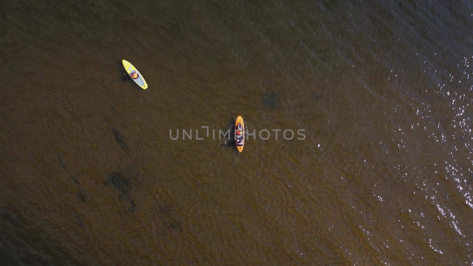 Two sapsurfers are floating on the river. Young people float on the boards top view. Drone view. 4k
