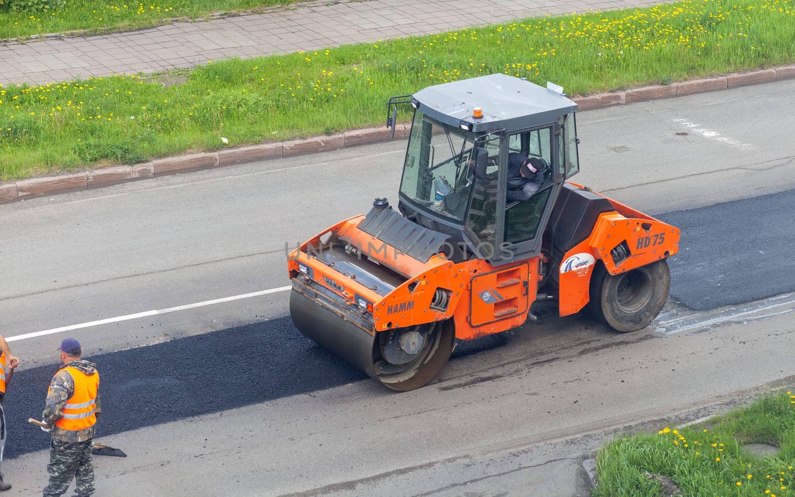 11.06.2022. Kemerovo, Russia. Road works on asphalt laying. Workers in vests are laying patches and rolling them out with a large roller.