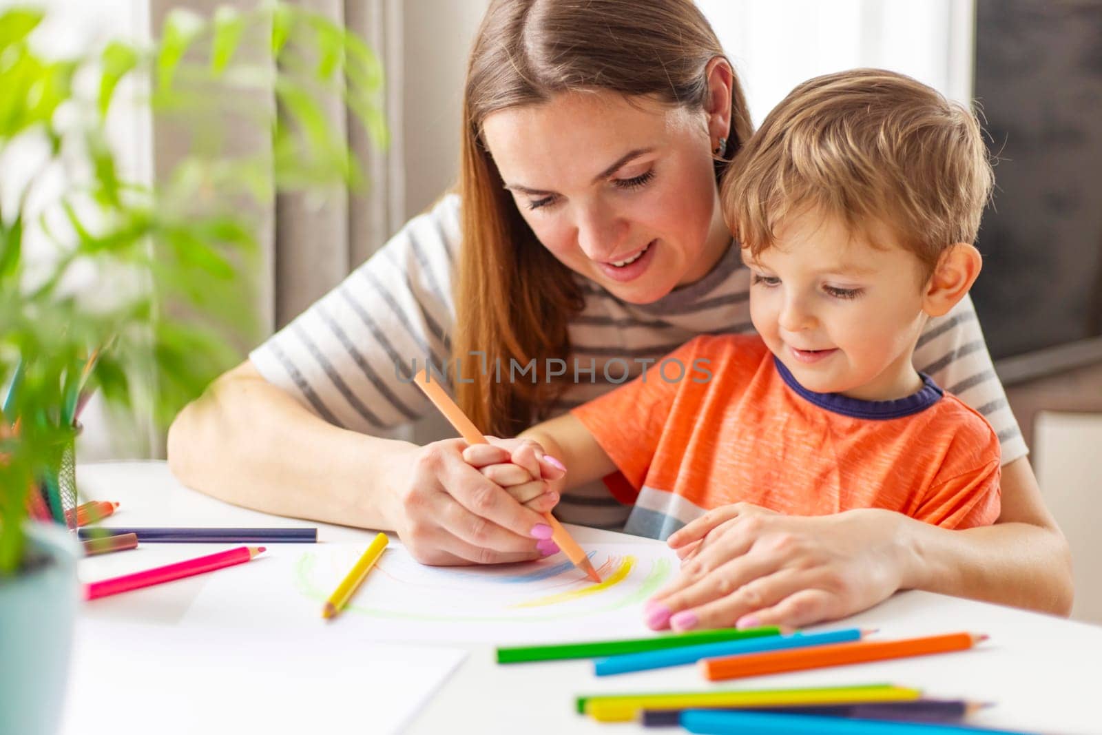 Happy family concept. Mother and her son drawing together. An adult woman helps a boy paint.