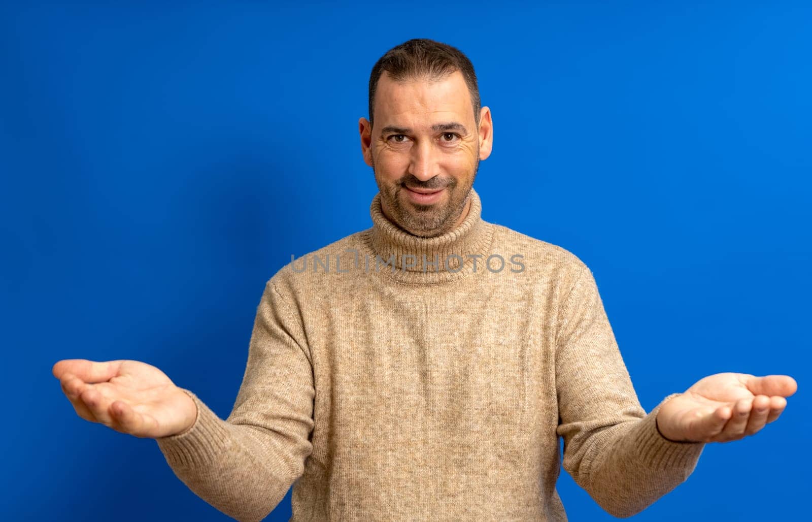 Bearded hispanic man in his 40s over blue background looking at the camera smiling with open arms for a hug. Cheerful expression embracing happiness.