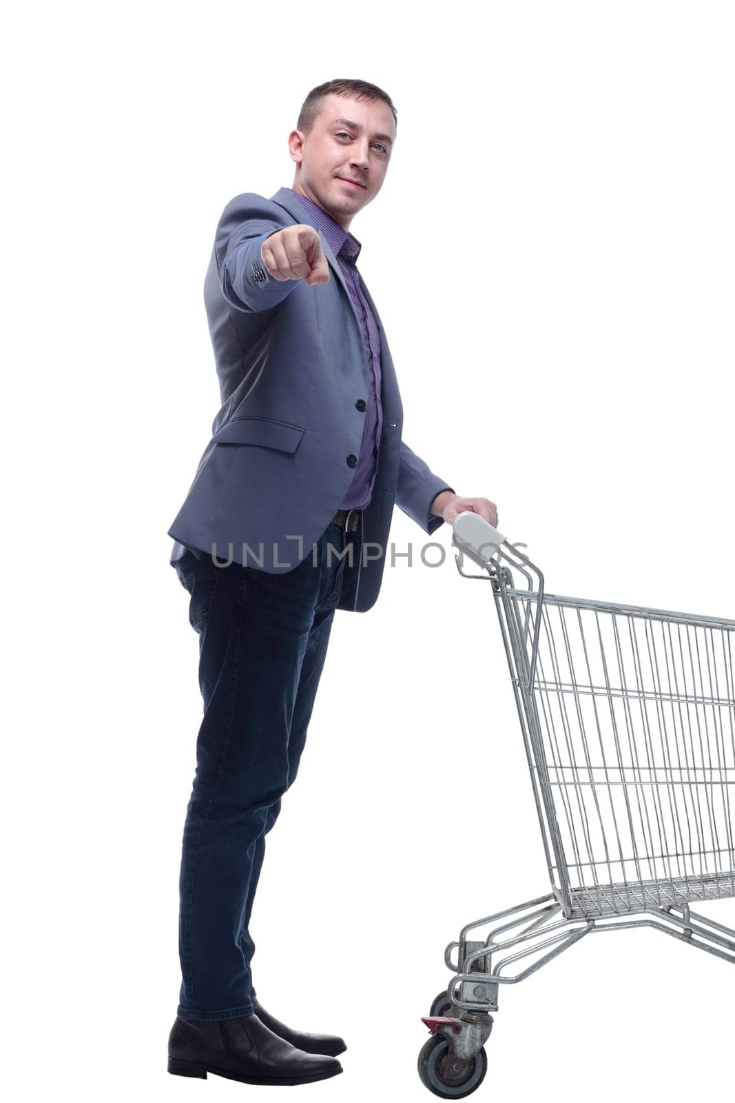 Full length view of handsome young man standing with shopping trolley and looking at camera isolated on white