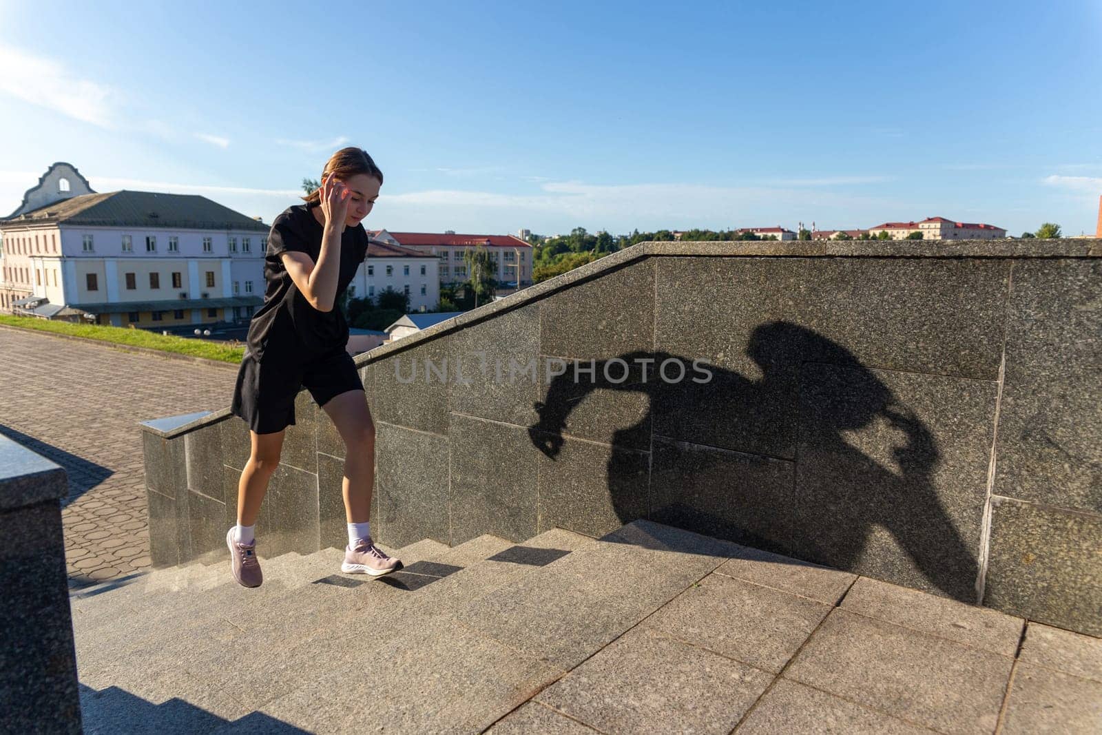 A young woman in black clothes running on stairs at city street early morning.