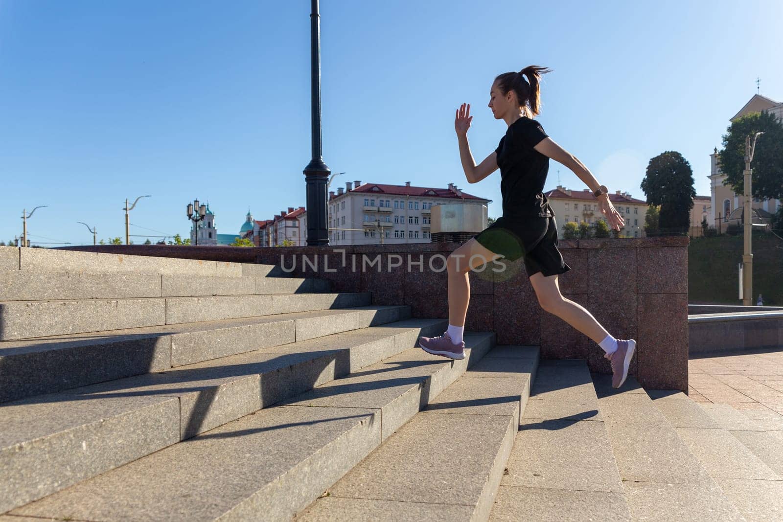A young woman in black clothes running on stairs at city street early morning.