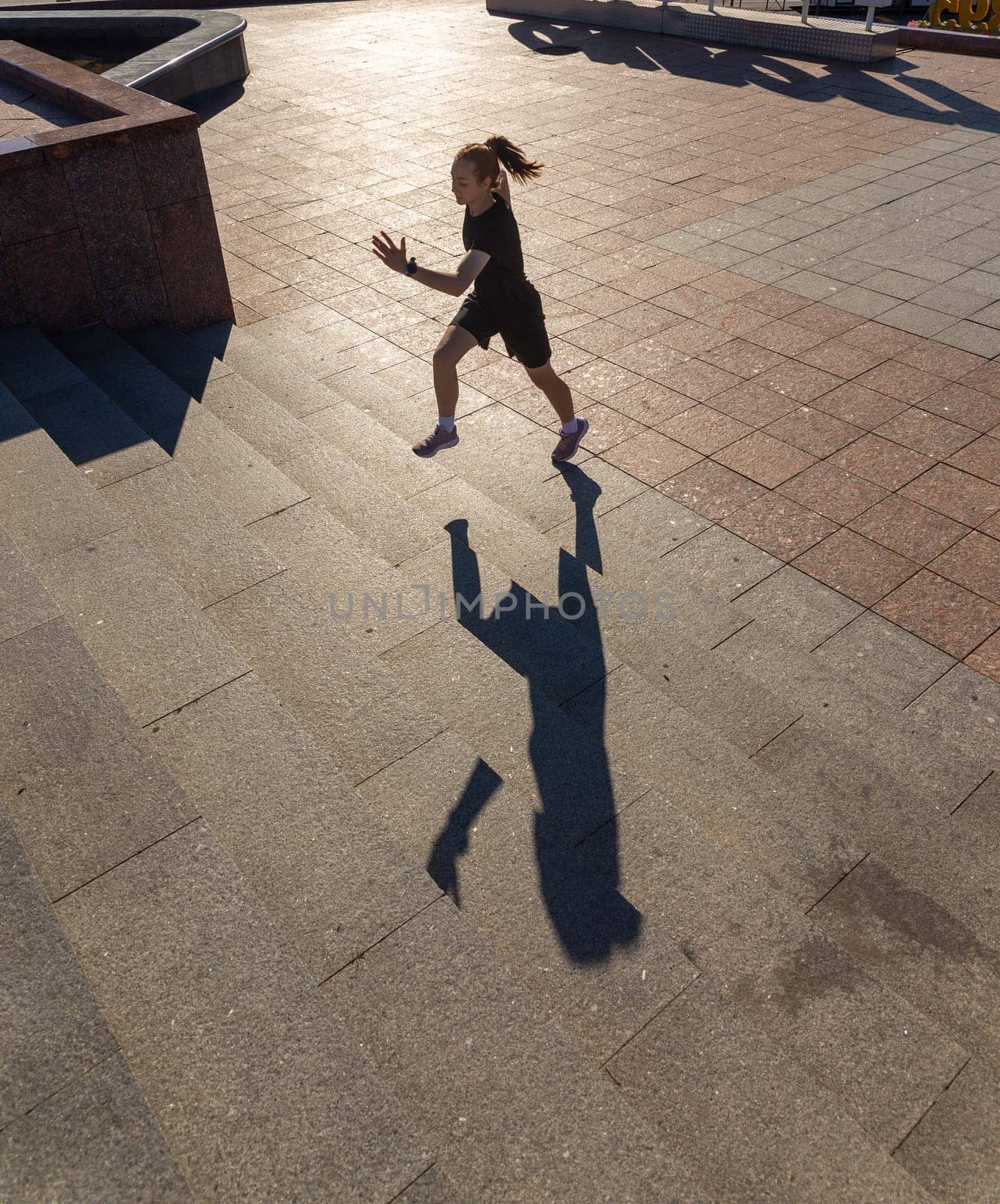 A young woman in black clothes running on stairs at city street early morning.