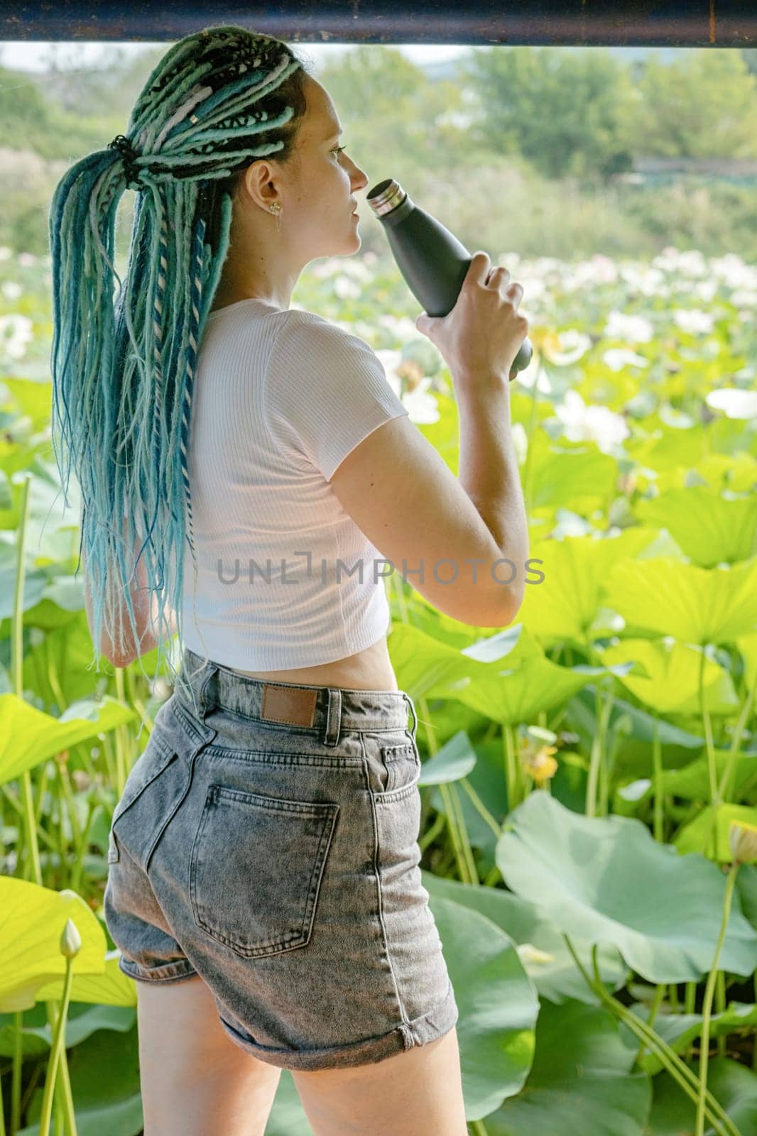 young beautiful woman with blue afro locks drinking water on wooden pierce on lotus lake enjoying nature
