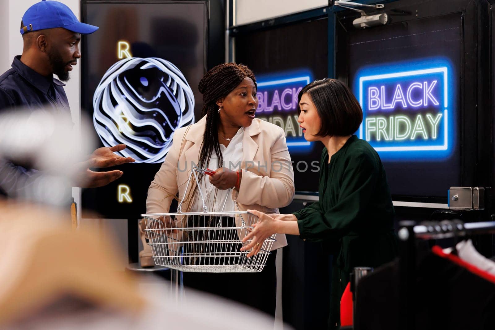 Two women shoppers battling over shopping basket in fashion mall. Security guard in uniform calming aggressive customers compete for deeply discounted clothes during Black Friday sales