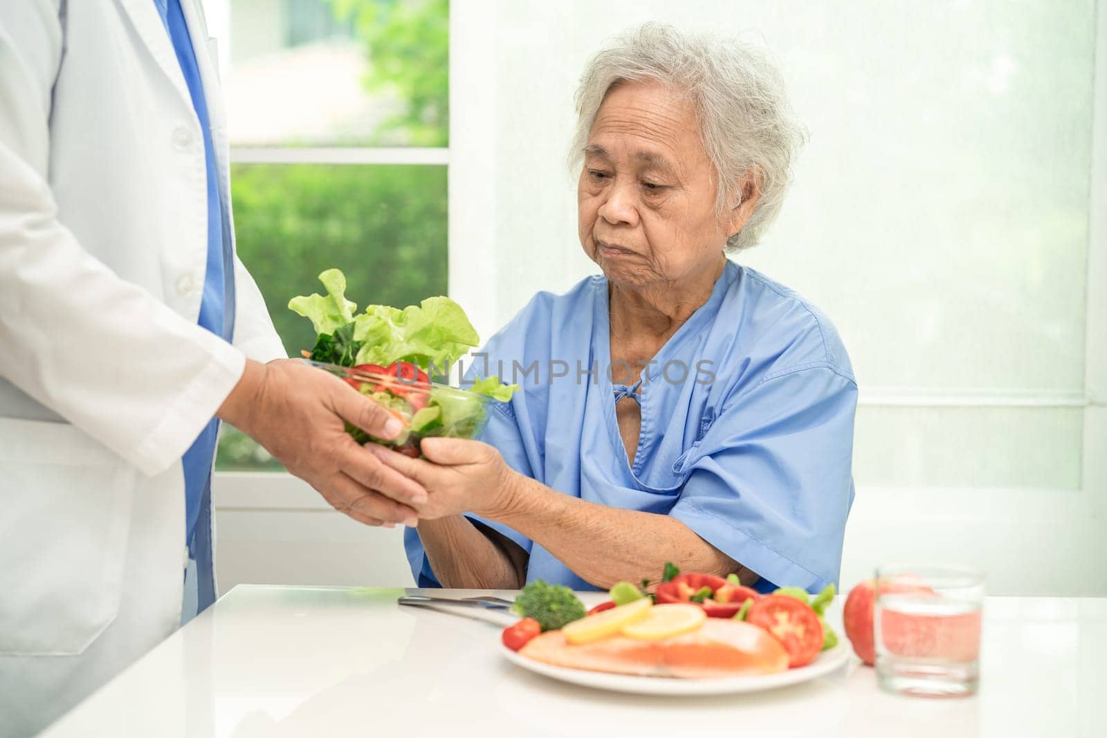 Asian elderly woman patient eating salmon steak breakfast with vegetable healthy food in hospital.