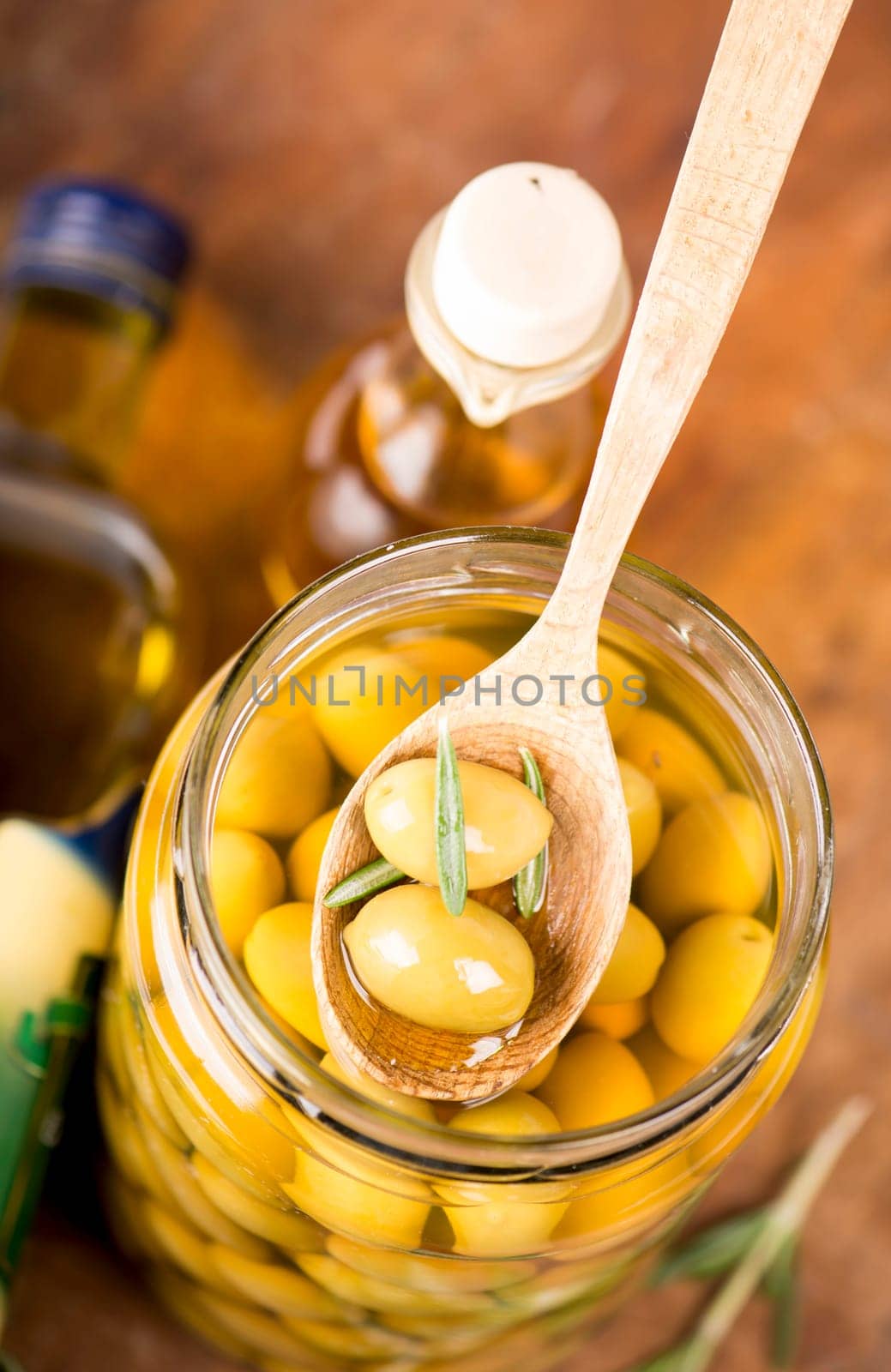 Close up green olives in wooden spoon, rosemary on a wooden background by aprilphoto