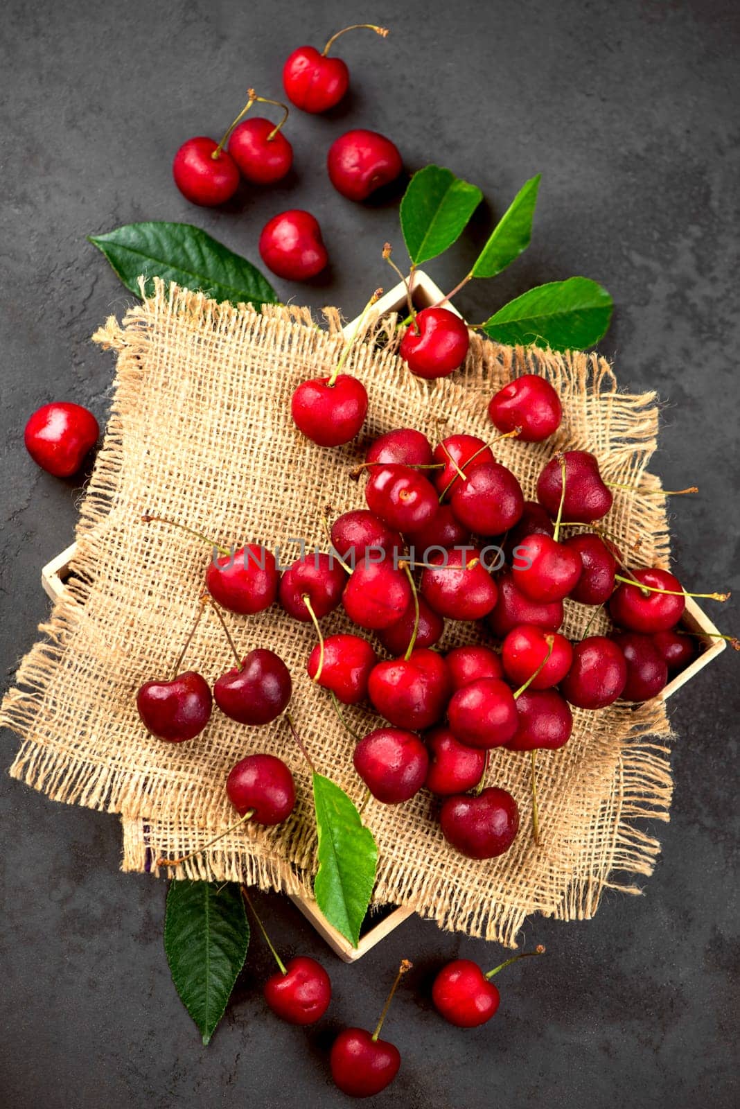 Sweet red cherry on burlap on a black background. A large number of cherries with leaves on the table, on a black background. close-up. by aprilphoto