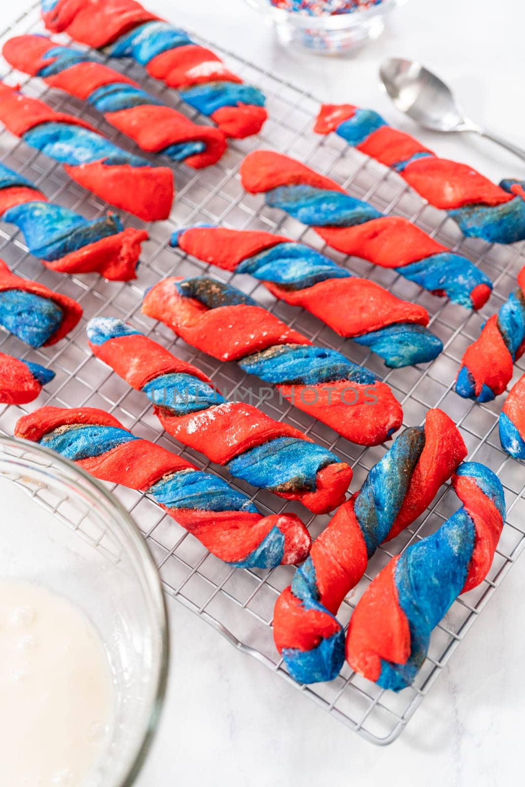 Drizzling white glaze on top of patriotic cinnamon twists. and decorating with star sprinkles.