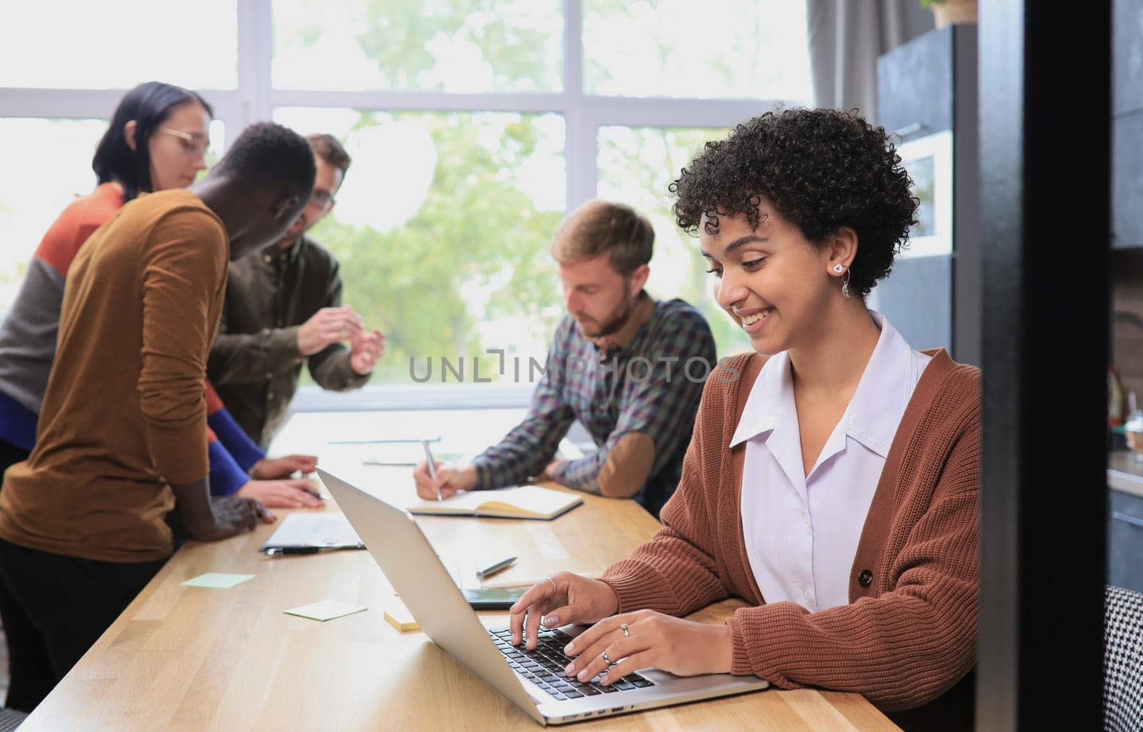 Businesswoman using laptop in office with team in background by asdf