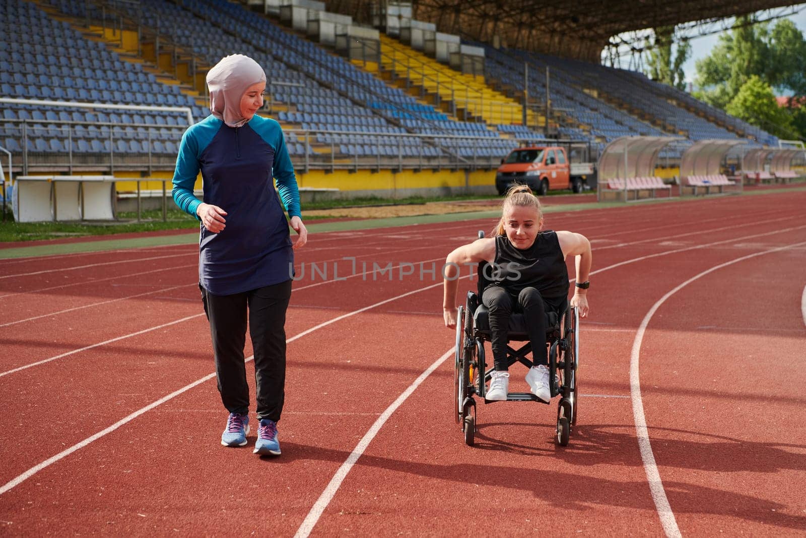 A Muslim woman in a burqa running together with a woman in a wheelchair on the marathon course, preparing for future competitions