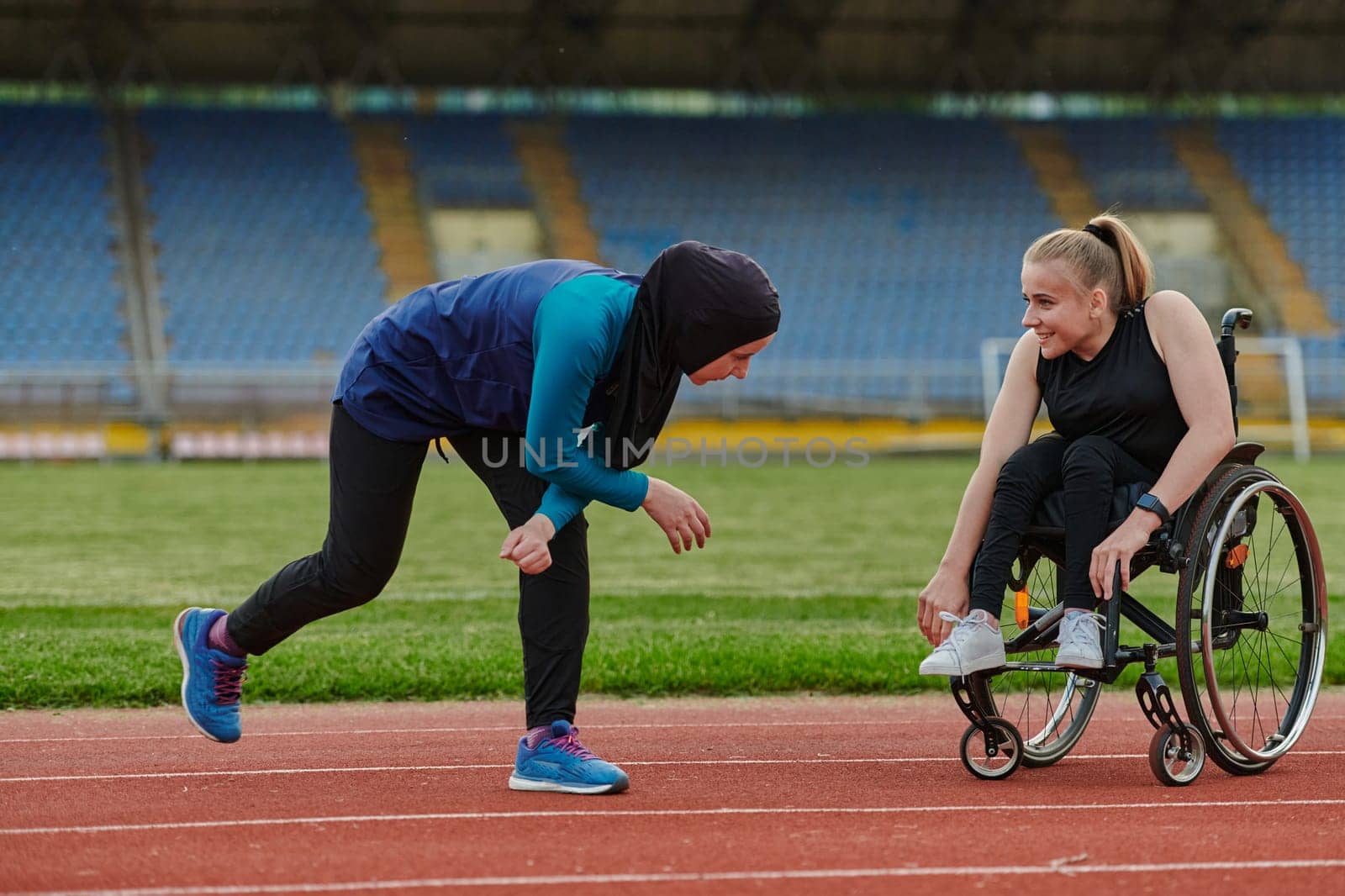 Two strong and inspiring women, one a Muslim wearing a burka and the other in a wheelchair stretching and preparing their bodies for a marathon race on the track.