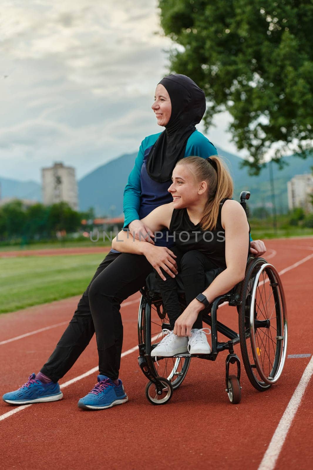 A Muslim woman wearing a burqa resting with a woman with disability after a hard training session on the marathon course by dotshock