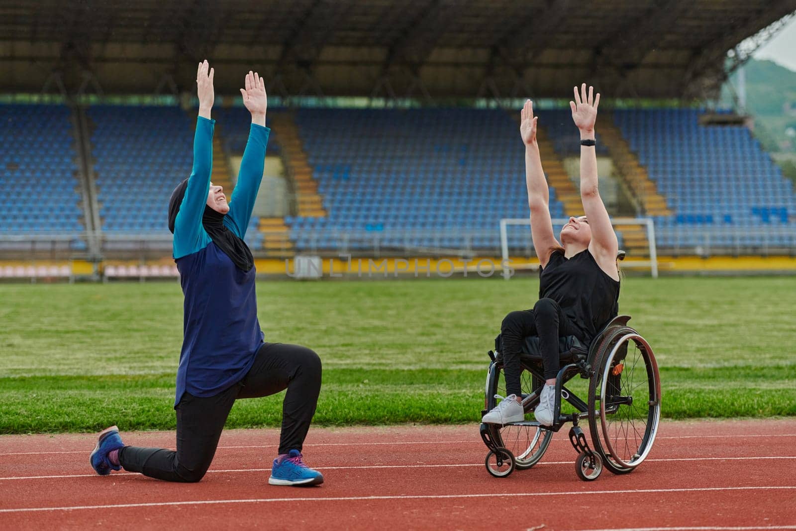 Two strong and inspiring women, one a Muslim wearing a burka and the other in a wheelchair stretching and preparing their bodies for a marathon race on the track.