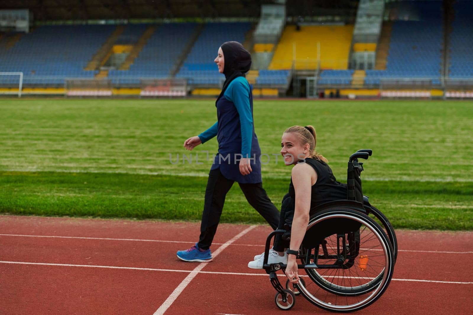 A Muslim woman in a burqa running together with a woman in a wheelchair on the marathon course, preparing for future competitions