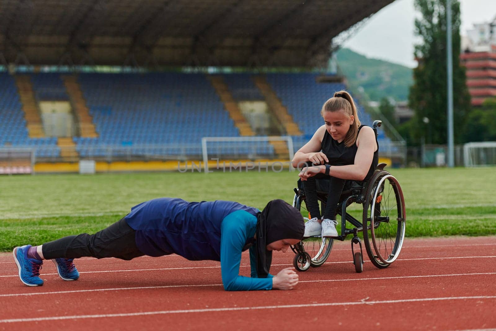 Two strong and inspiring women, one a Muslim wearing a burka and the other in a wheelchair stretching and preparing their bodies for a marathon race on the track.