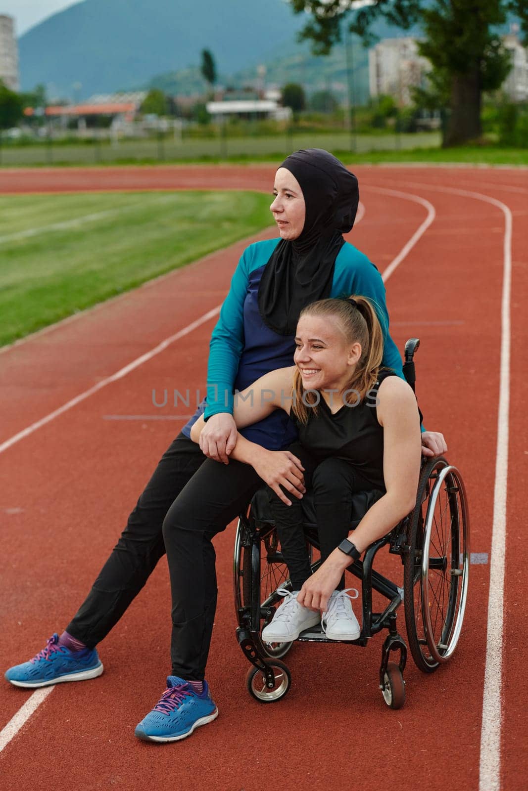 A Muslim woman wearing a burqa resting with a woman with disability after a hard training session on the marathon course.