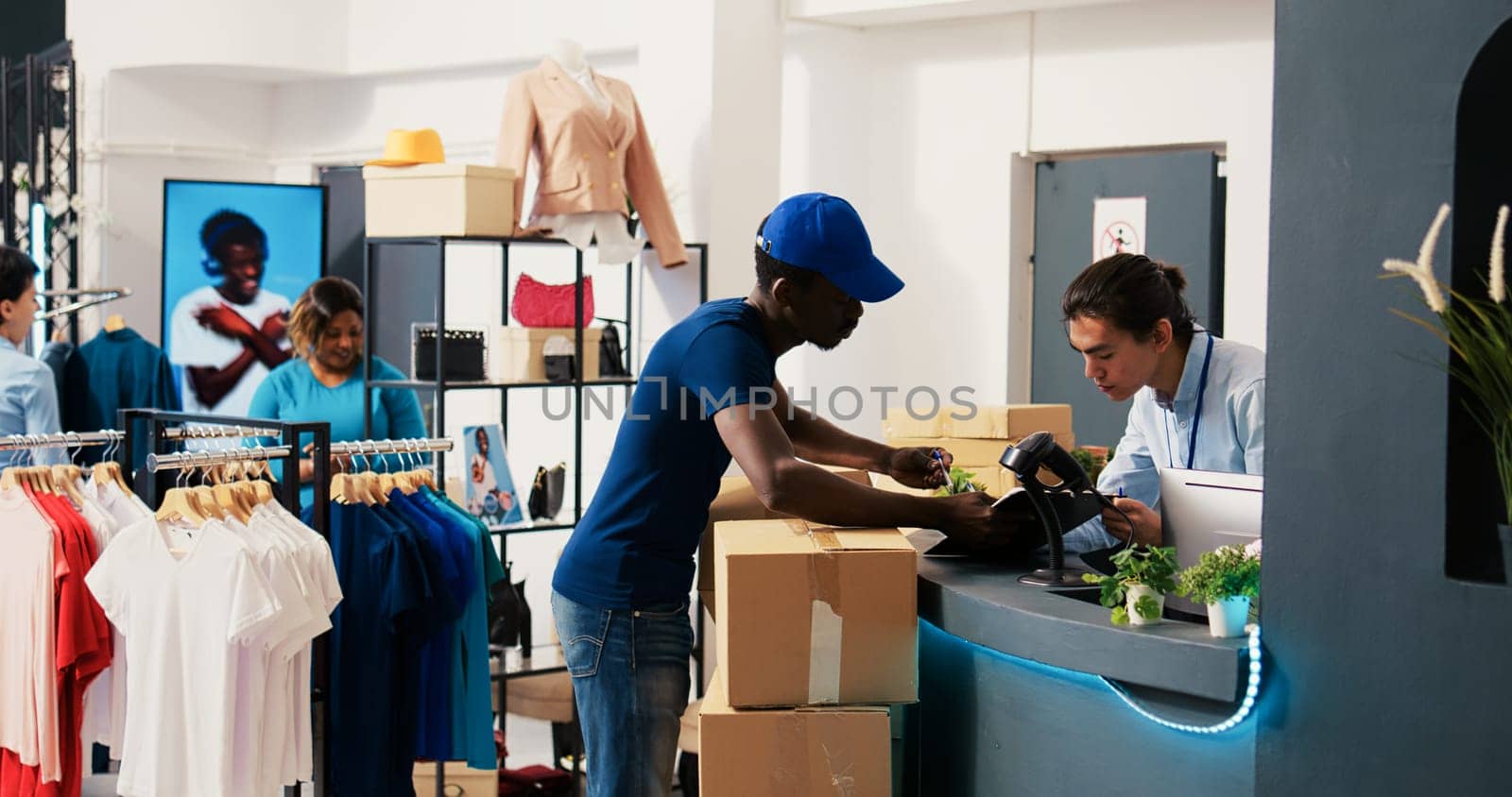 African american courier putting worker to sign delivey report, discussing customers shipping detalis in modern boutique. Deliveryman taking cardboard boxes, preparing to ship packages to clients