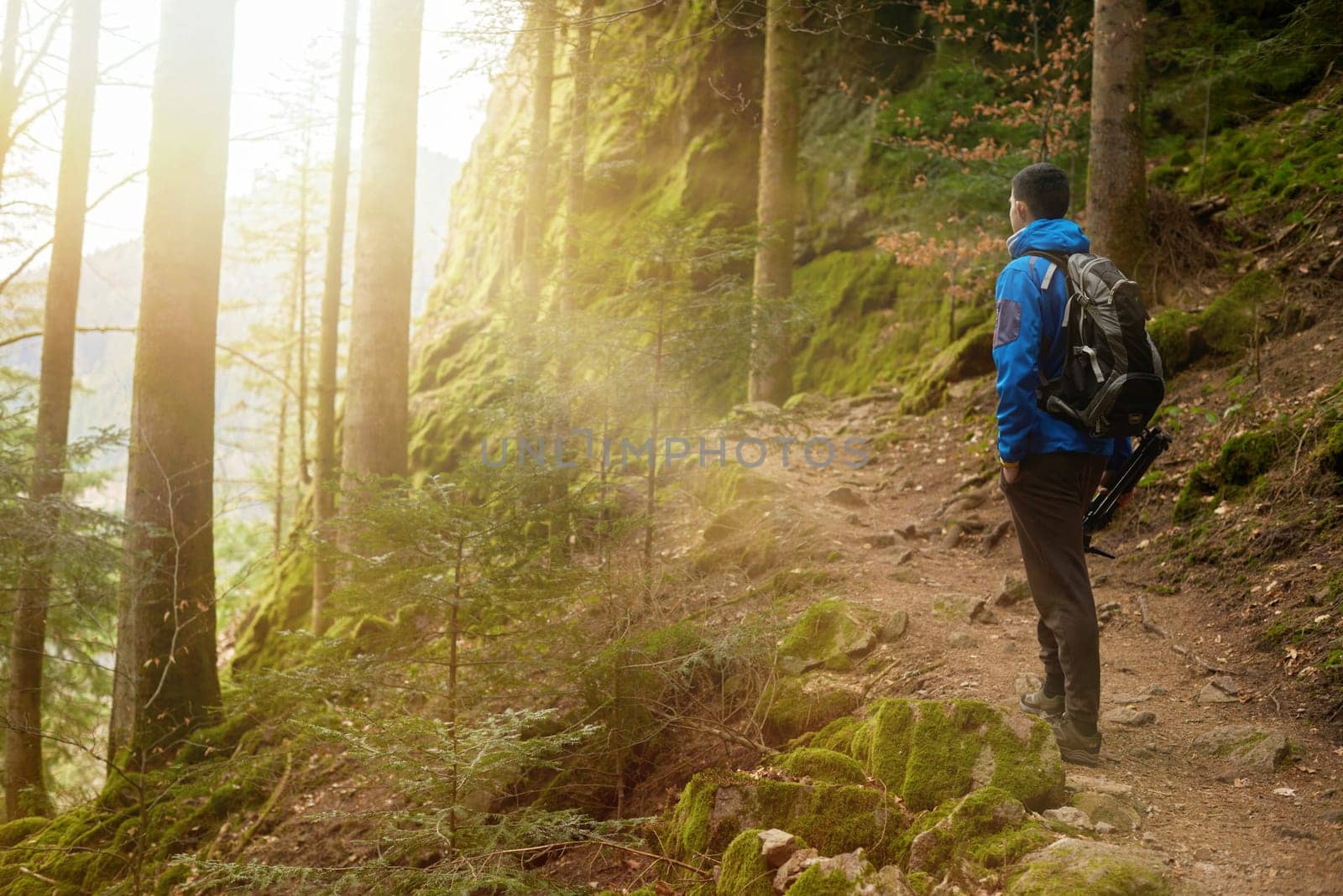 A guy tourist with a backpack stands on a mountain trail and looks into the distance. The concept of travel and adventure. Traveler Man with backpack mountaineering Travel Lifestyle concept mountains on background Summer trip vacations outdoor. Concept of travel and healthy, active lifestyle. Young guy with dreadlocks went hiking in mountains. Man with yellow backpack stands on top of hill and enjoys views of nature.