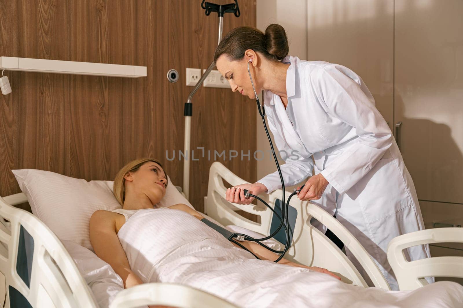 Doctor checking blood pressure of sick woman patient in ward of modern clinic. High quality photo