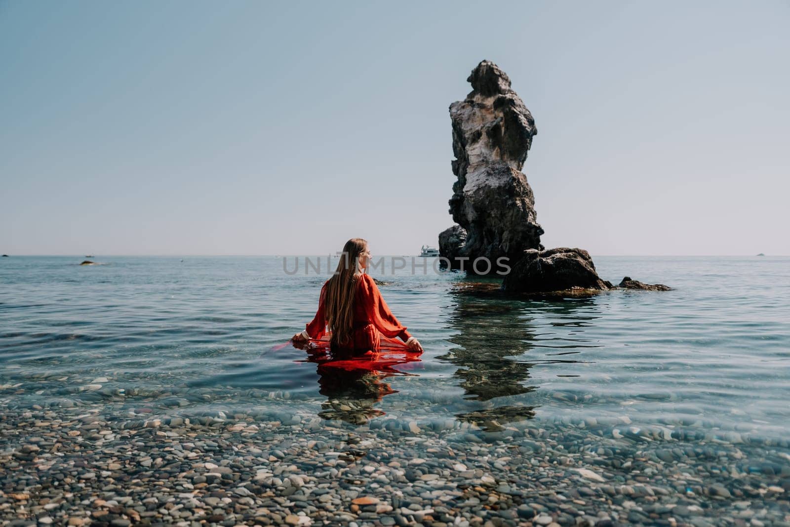 Woman travel sea. Happy tourist in red dress enjoy taking picture outdoors for memories. Woman traveler posing on the rock at sea bay surrounded by volcanic mountains, sharing travel adventure journey by panophotograph