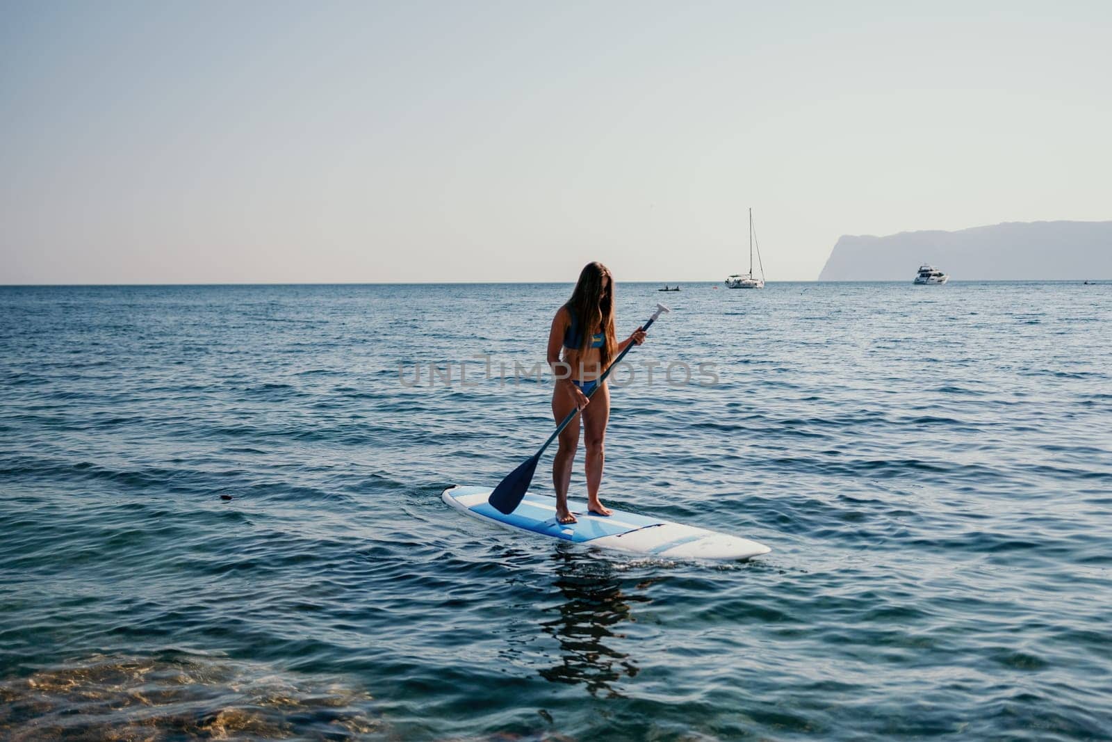 Close up shot of happy young caucasian woman looking at camera and smiling. Cute woman portrait in bikini posing on a volcanic rock high above the sea