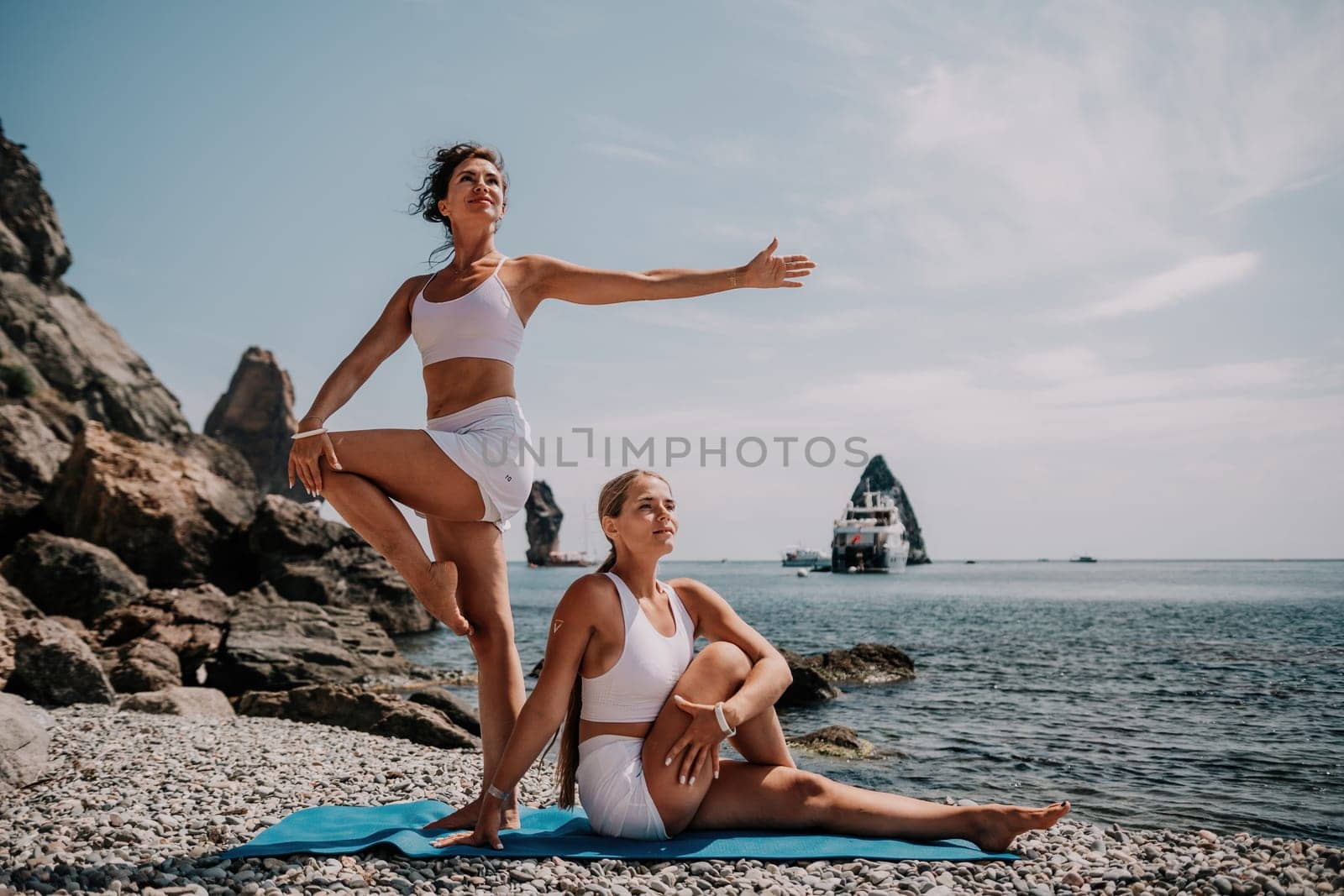 Woman sea yoga. Two Happy women meditating in yoga pose on the beach, ocean and rock mountains. Motivation and inspirational fit and exercising. Healthy lifestyle outdoors in nature, fitness concept. by panophotograph