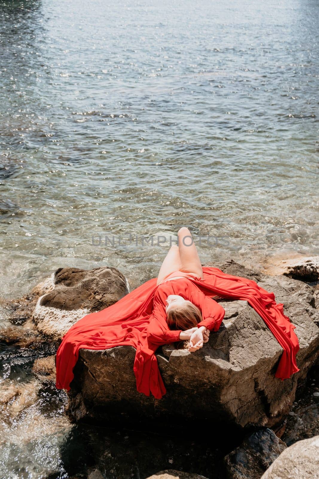 Woman travel sea. Young Happy woman in a long red dress posing on a beach near the sea on background of volcanic rocks, like in Iceland, sharing travel adventure journey