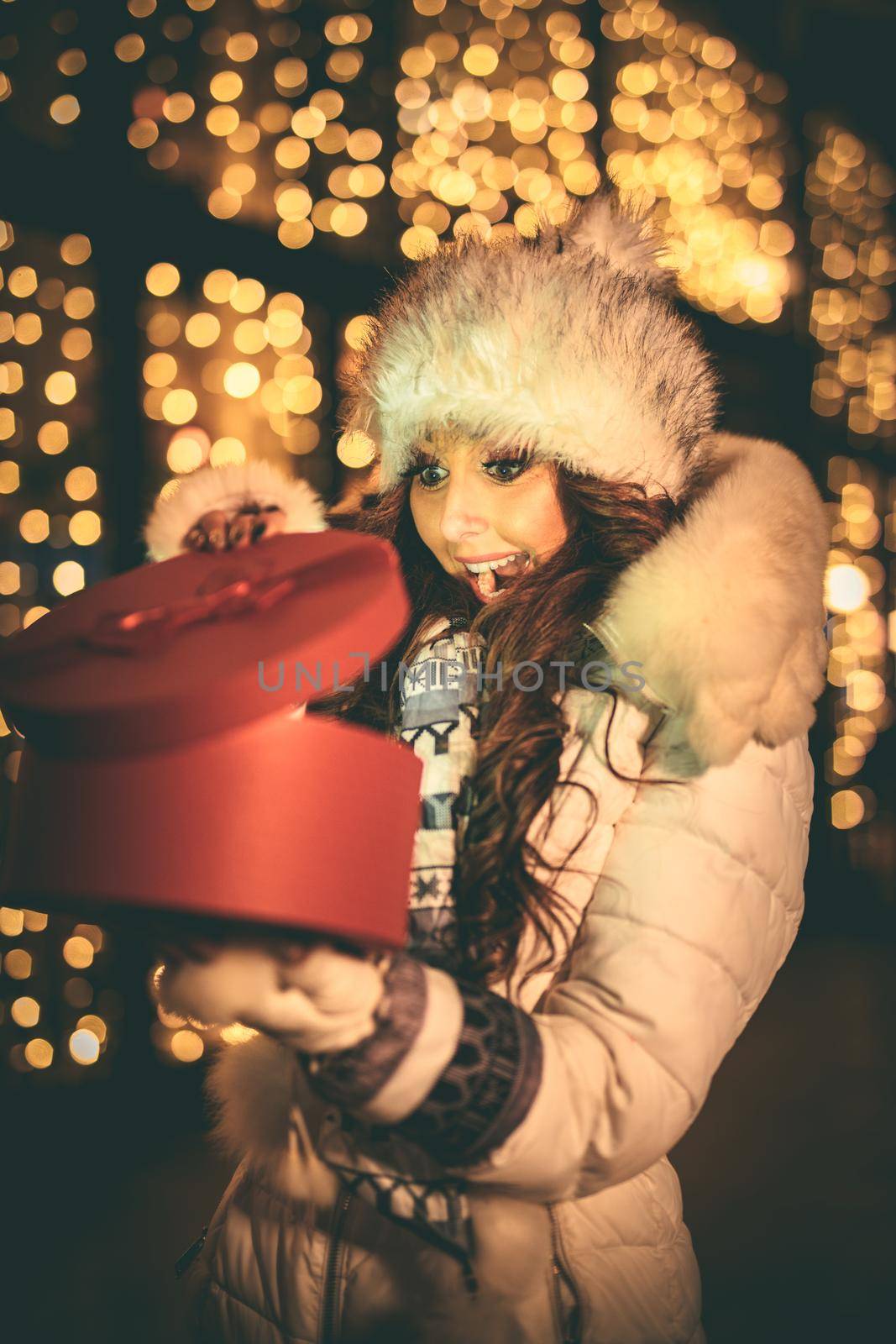 Cheerful young woman with red present having fun in the city street at Christmas time.