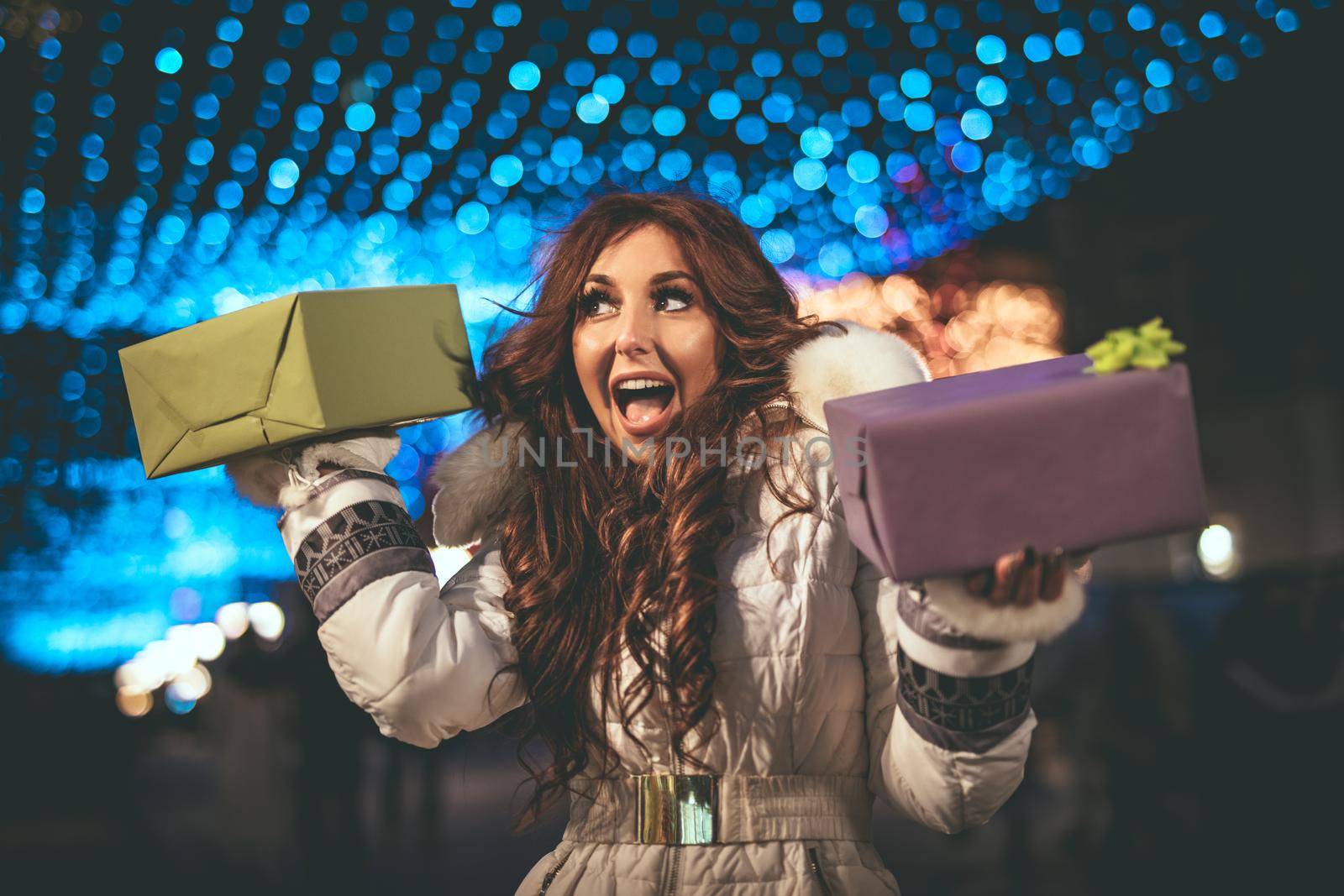 Cheerful young woman with present having fun in the city street at the Christmas time.