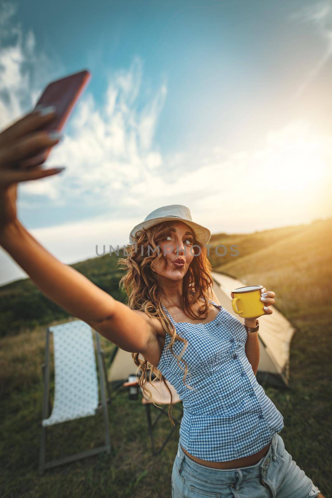 Happy young woman enjoys a nice day in nature. She's smiling and taking selfie with smartphone.