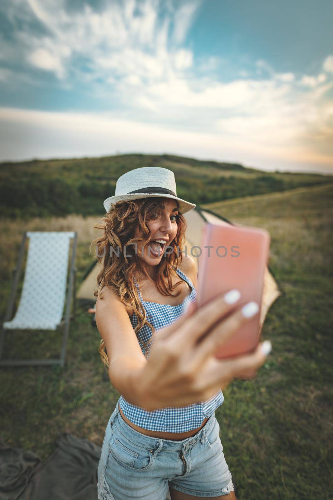 Happy young woman enjoys a nice day in nature. She's smiling and taking selfie with smartphone.