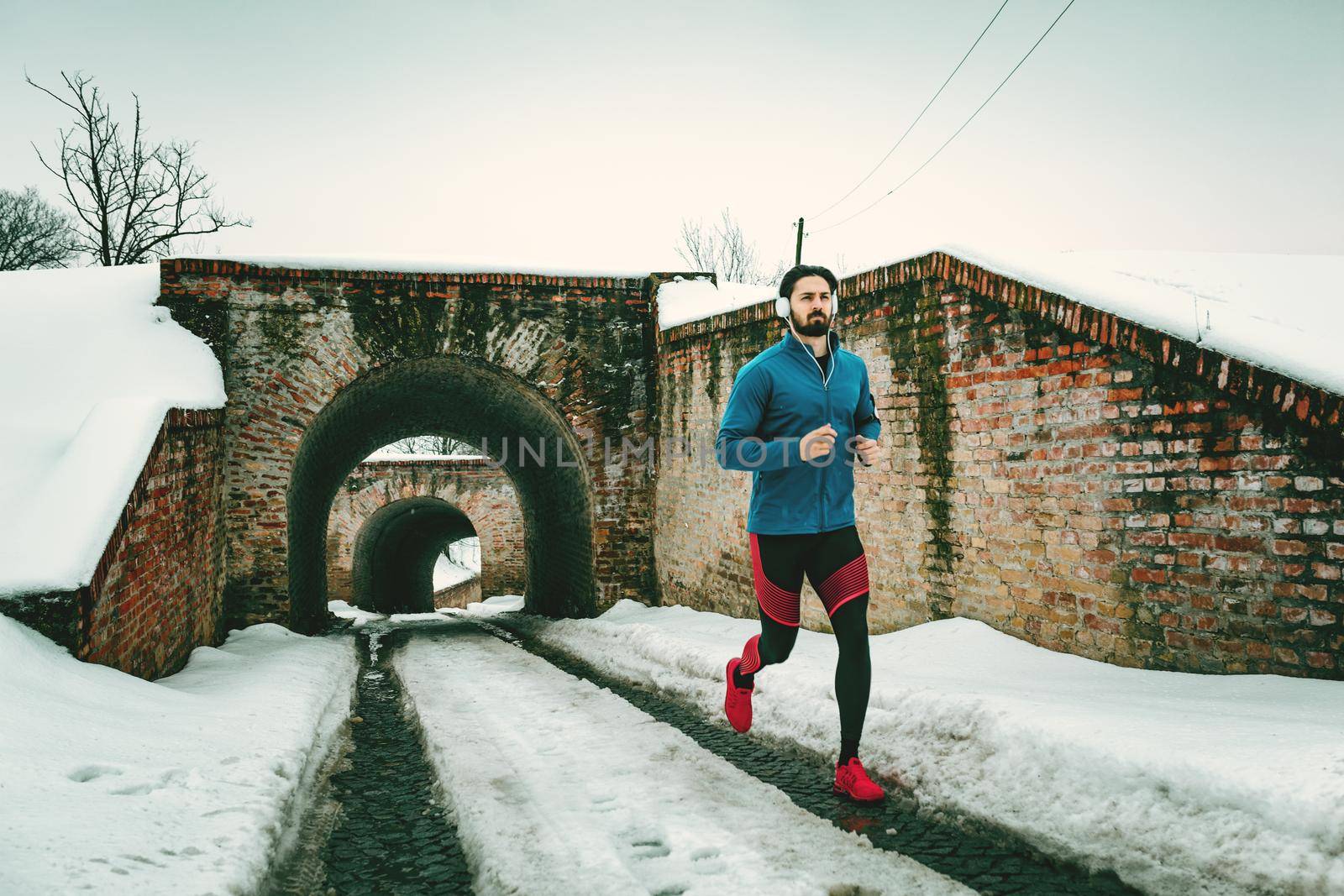 A male runner with headphones on his ears running in the public place during the winter training outside in. Copy space.