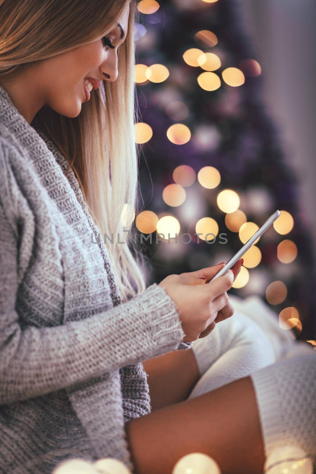 Cute young smiling woman using smarthphone and smiling during cozy Xmas holidays at home.
