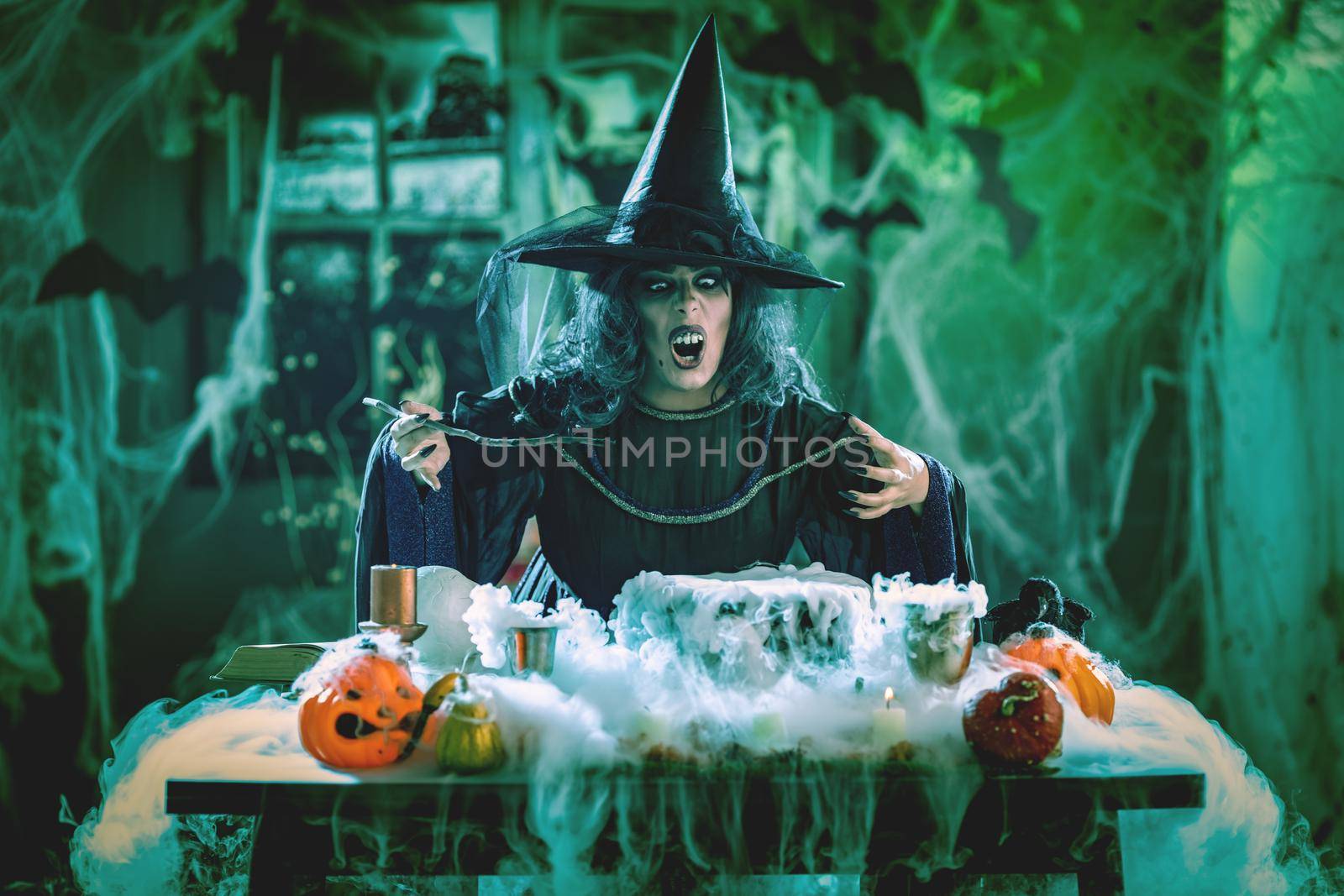 Witch with awfully face and hat on her head in creepy surroundings full of cobweb sends evil. Halloween concept.