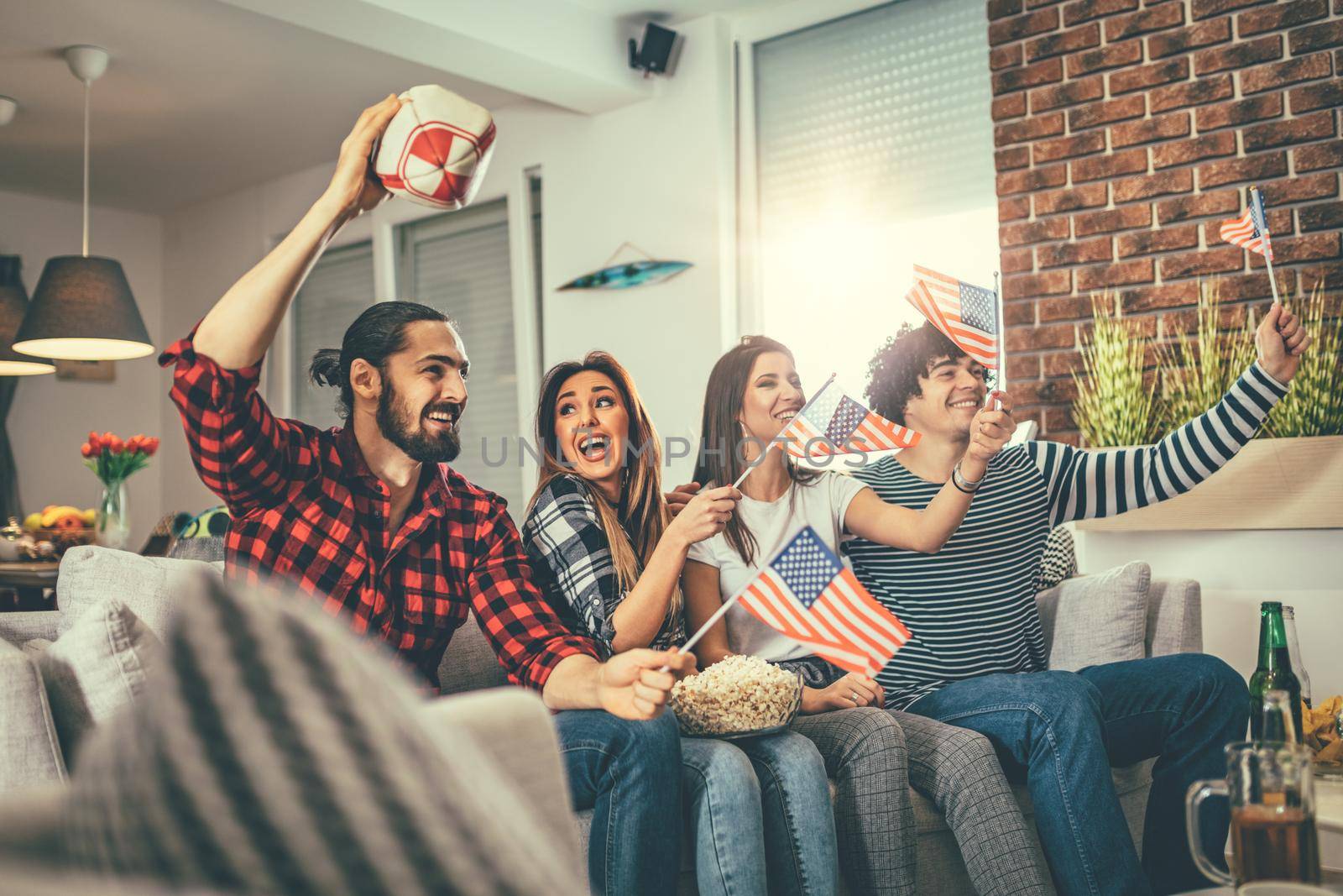 Friends are fans of sports games as American football love spending their free time at home together. They are screaming and gesturing for a victory. 